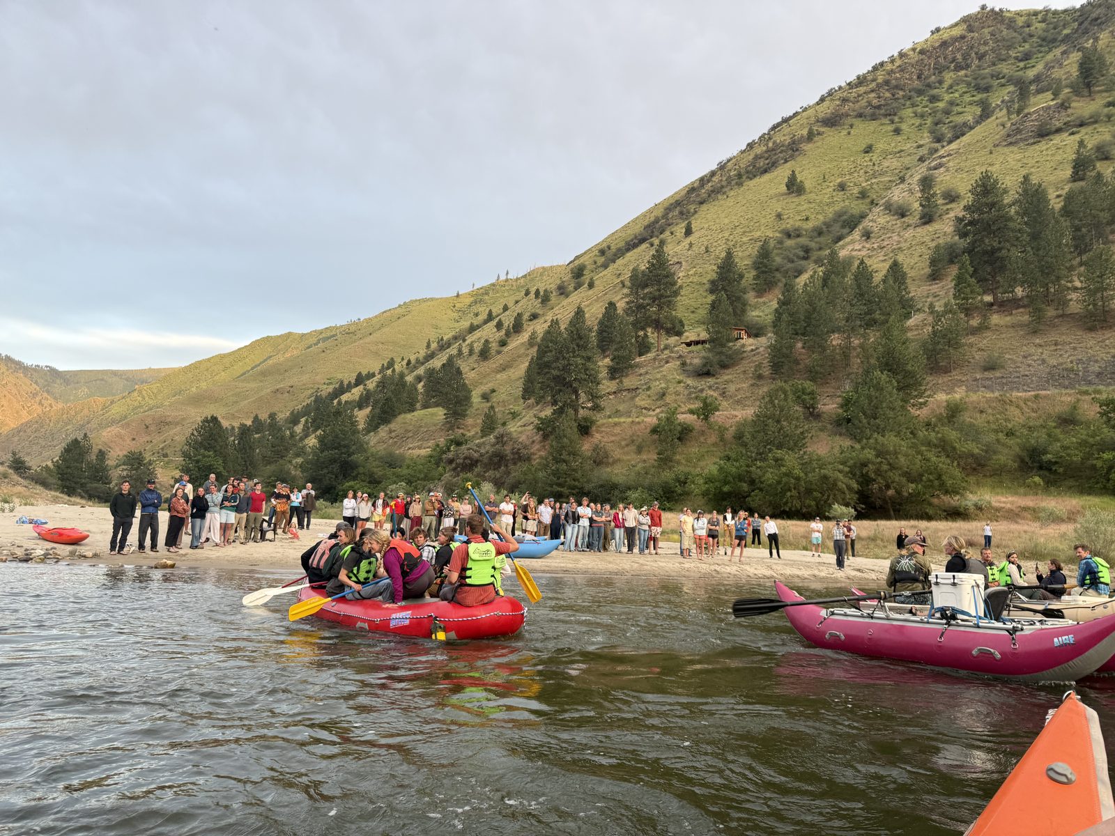 Friends and family at the water's edge with kayaks and rafts, canyon walls behind