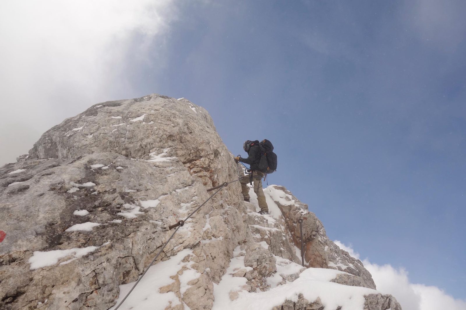 Scott climbing a snowy ridge with via ferrata cables, alone against the sky