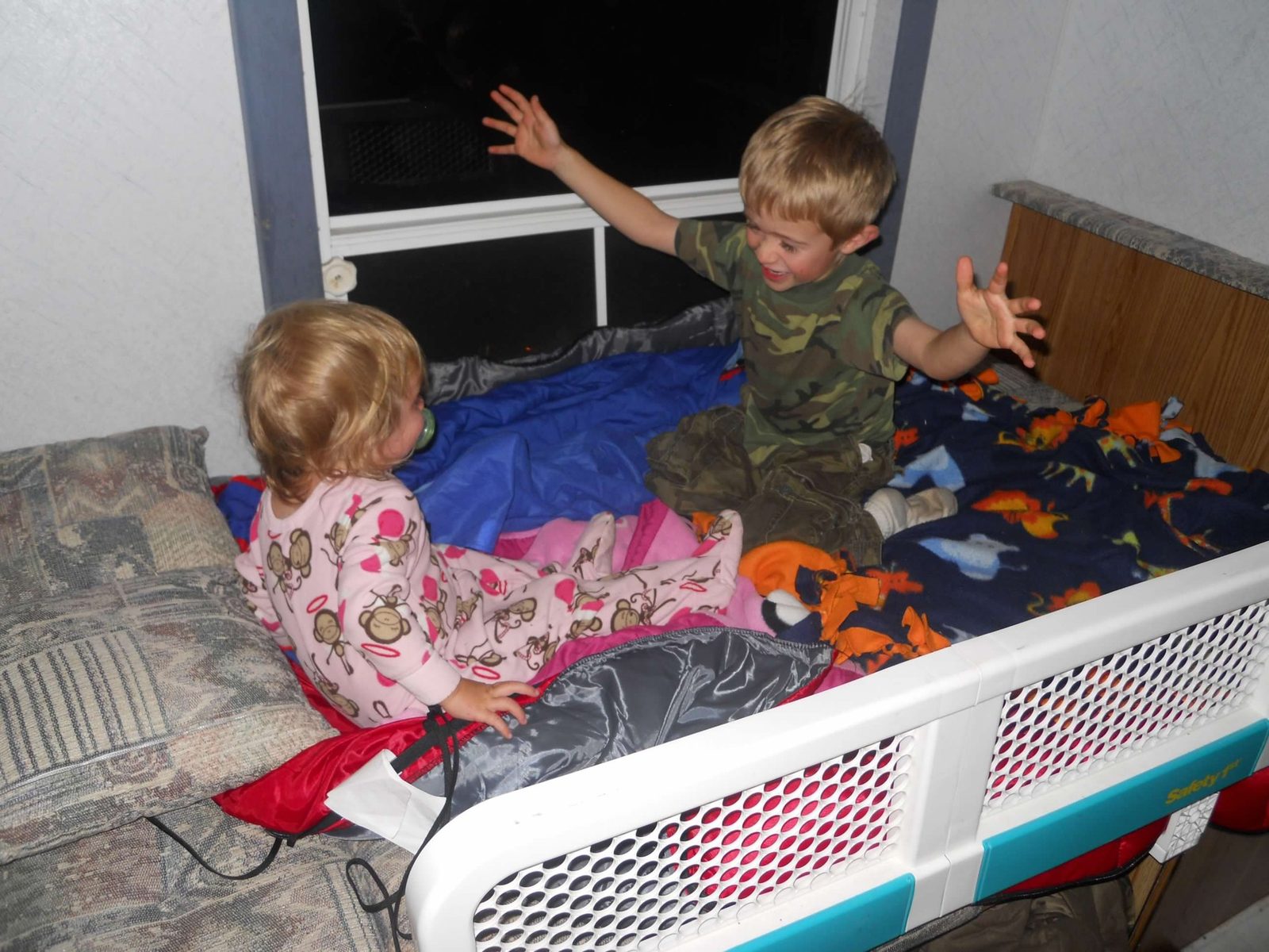 Little Scott in camo and his sister Kate in pajamas, both with hands in the air laughing