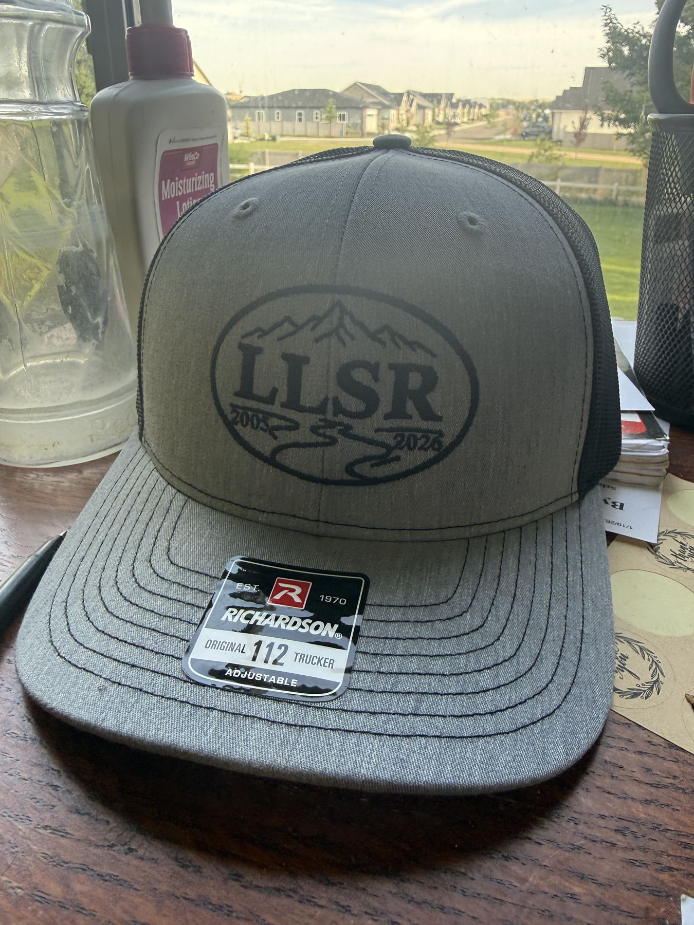 The Live Like Scott Robbins hat &mdash; 2005 to 2026 &mdash; tag still on, waiting on the table before the trip
